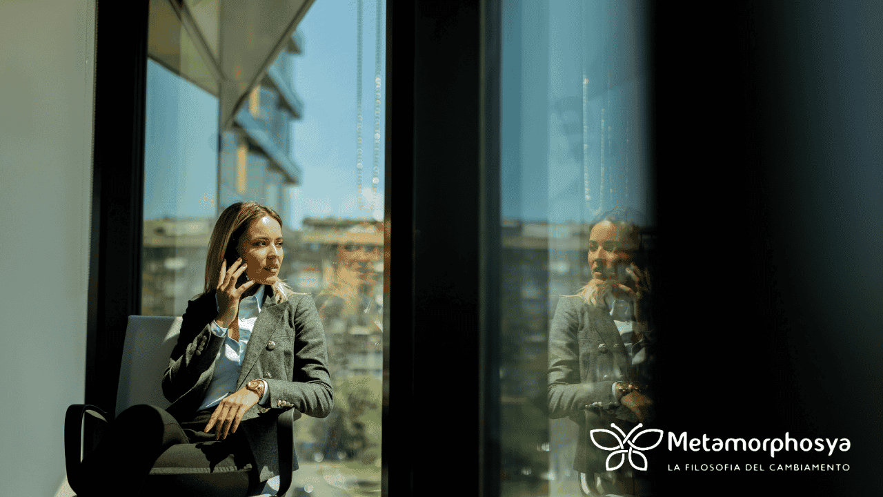 Professionista al telefono accanto a una vetrata, con il suo riflesso visibile: un'immagine della trappola del tempo tra lavoro e libertà personale.
